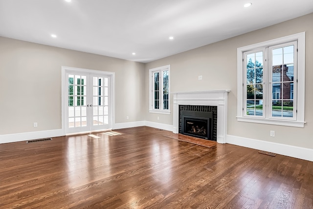 unfurnished living room featuring hardwood / wood-style floors, a brick fireplace, and french doors