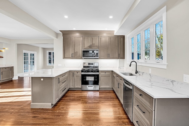 kitchen featuring light stone countertops, sink, stainless steel appliances, dark hardwood / wood-style flooring, and kitchen peninsula