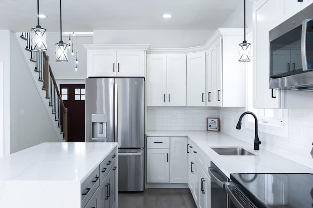 kitchen featuring stainless steel appliances, a sink, white cabinetry, backsplash, and pendant lighting