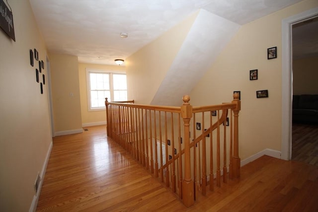 hallway with baseboards, an upstairs landing, and wood finished floors