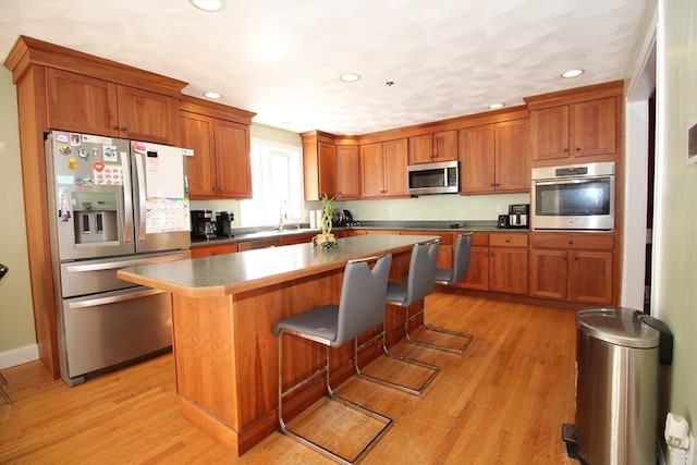 kitchen with light wood-type flooring, stainless steel appliances, a kitchen island, and brown cabinetry