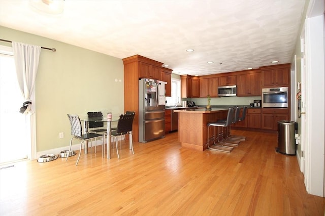 kitchen with light wood-style flooring, appliances with stainless steel finishes, a kitchen island, and a kitchen breakfast bar