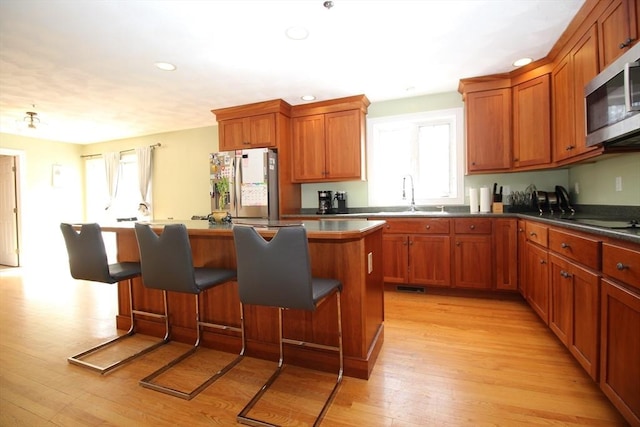 kitchen with a center island, a kitchen bar, light wood-type flooring, appliances with stainless steel finishes, and a sink