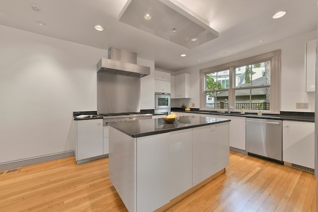 kitchen with a center island, stainless steel appliances, wall chimney exhaust hood, white cabinets, and light hardwood / wood-style flooring