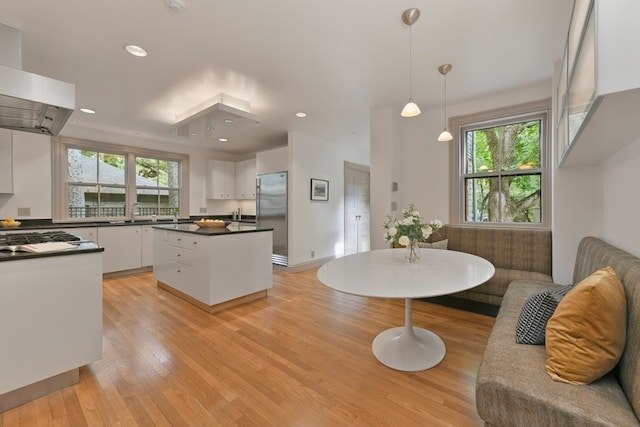 kitchen featuring light hardwood / wood-style floors, pendant lighting, white cabinets, stainless steel refrigerator, and exhaust hood