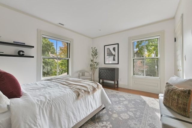 bedroom featuring ornamental molding, multiple windows, and light wood-type flooring