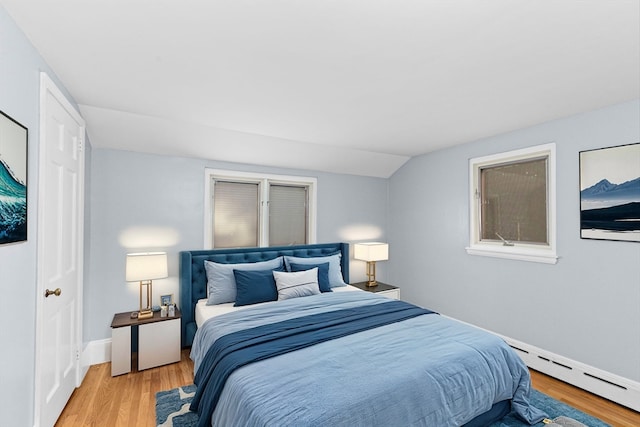 bedroom with light hardwood / wood-style floors, vaulted ceiling, and a baseboard heating unit