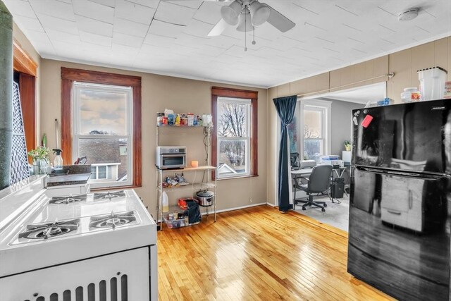 kitchen with white gas stove, black refrigerator, ornamental molding, ceiling fan, and light hardwood / wood-style floors