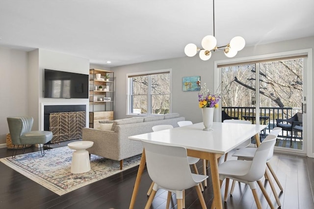 dining space featuring a fireplace with flush hearth, dark wood-type flooring, and an inviting chandelier