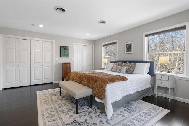 bedroom with baseboards, dark wood finished floors, visible vents, and multiple closets