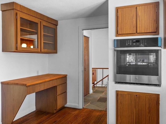 104 Tower Rd, Lincoln, MA 01773 - kitchen featuring brown cabinets, oven, baseboards, dark wood-style floors, and glass insert cabinets