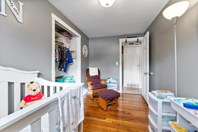 bedroom featuring a closet, a barn door, a textured ceiling, and light hardwood / wood-style flooring