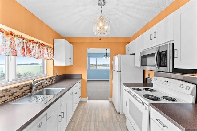 kitchen with a sink, white appliances, a notable chandelier, and plenty of natural light