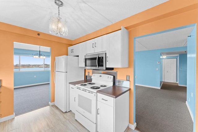 kitchen with dark countertops, a chandelier, light carpet, white appliances, and white cabinetry