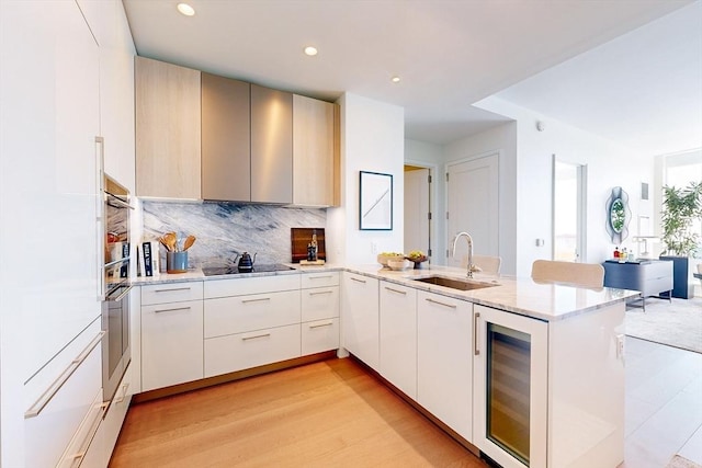 kitchen with kitchen peninsula, black electric stovetop, backsplash, beverage cooler, and sink