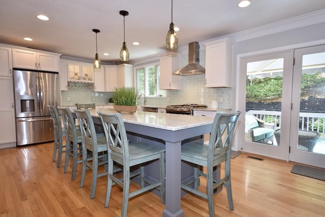 24 Sheppard Rd, Bourne, MA 02562 - kitchen featuring stainless steel appliances, wall chimney range hood, white cabinetry, a center island, and ornamental molding