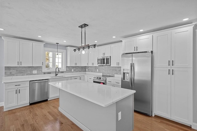 kitchen with appliances with stainless steel finishes, light wood-type flooring, pendant lighting, white cabinets, and a center island