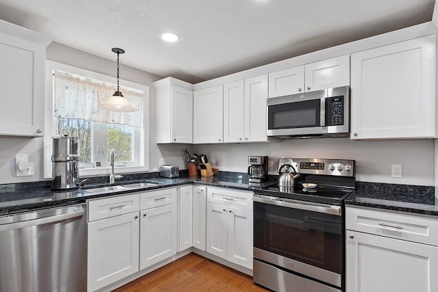 kitchen featuring decorative light fixtures, light wood finished floors, a sink, white cabinetry, and stainless steel appliances
