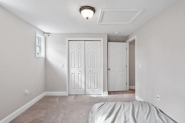 unfurnished bedroom featuring baseboards, a closet, attic access, and carpet floors