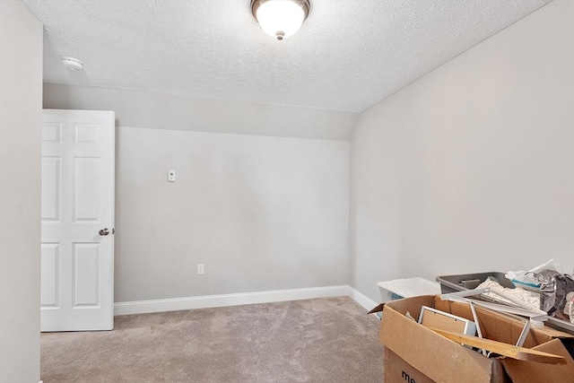 spare room with a textured ceiling, baseboards, and light colored carpet