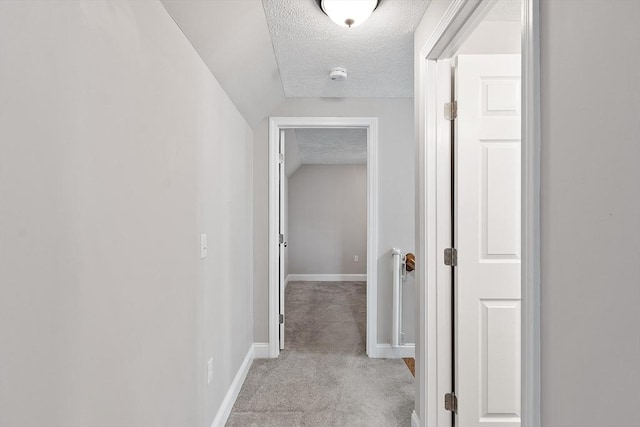 corridor featuring vaulted ceiling, light carpet, a textured ceiling, and baseboards