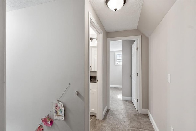 hall featuring baseboards, light carpet, an upstairs landing, and a textured ceiling