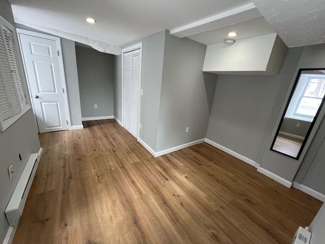 unfurnished bedroom featuring a baseboard radiator, a closet, baseboards, and wood finished floors