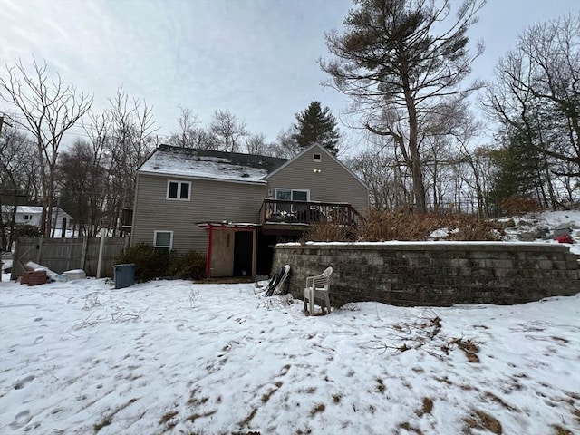 snow covered house with a wooden deck and fence