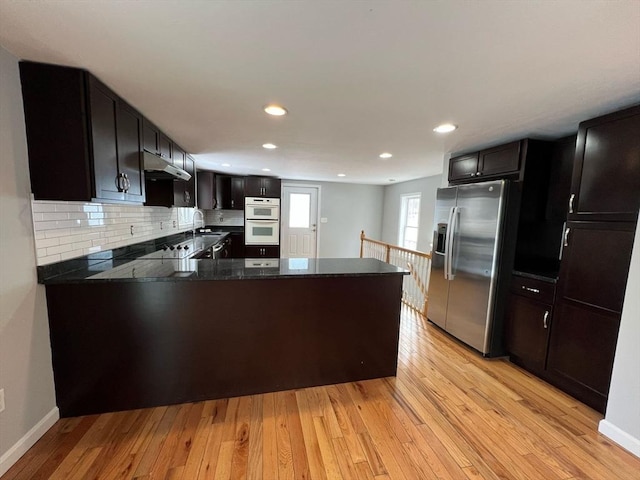 kitchen with a peninsula, under cabinet range hood, stainless steel fridge, and light wood-style floors