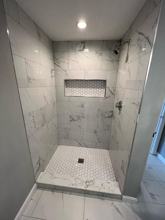 full bath featuring marble finish floor, a tile shower, and baseboards