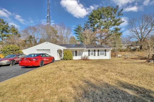 ranch-style house with an attached garage, solar panels, driveway, and a front yard