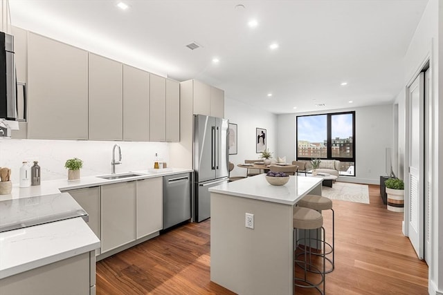 kitchen with wood finished floors, a kitchen island, a breakfast bar, a sink, and appliances with stainless steel finishes