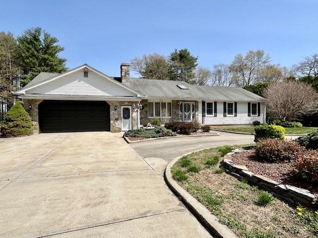 ranch-style home featuring curved driveway, a garage, stone siding, and a chimney