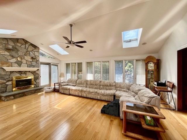 living room with a ceiling fan, a wealth of natural light, vaulted ceiling with skylight, and wood finished floors