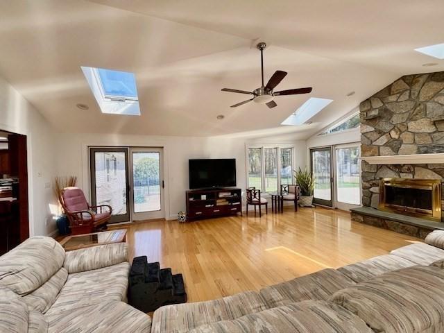 living area with a ceiling fan, wood finished floors, vaulted ceiling with skylight, and a fireplace