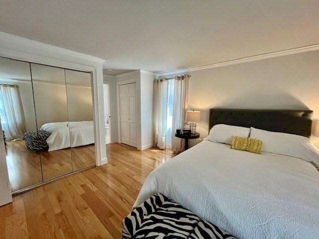 bedroom featuring multiple closets, ornamental molding, baseboards, and light wood-style flooring