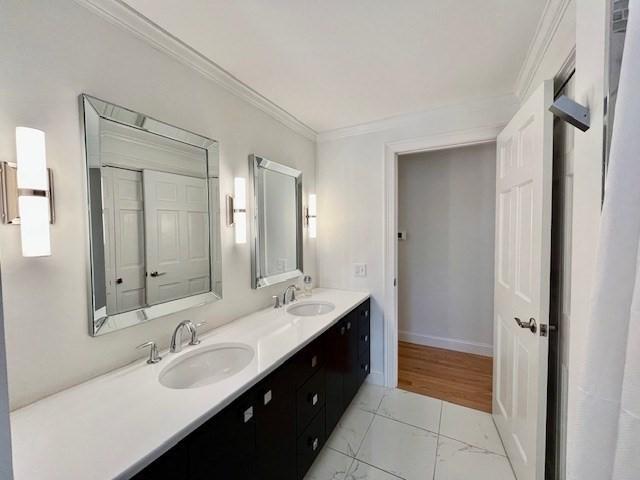 bathroom featuring crown molding, double vanity, a sink, and marble finish floor