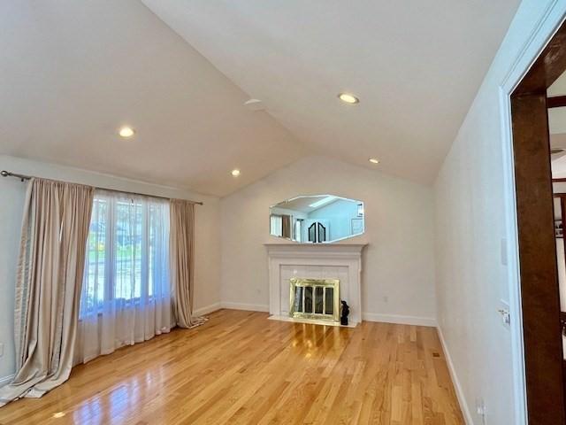 unfurnished living room featuring a fireplace, vaulted ceiling, wood finished floors, baseboards, and recessed lighting