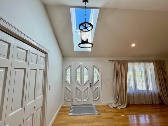 foyer featuring vaulted ceiling, light wood finished floors, a chandelier, and a wealth of natural light