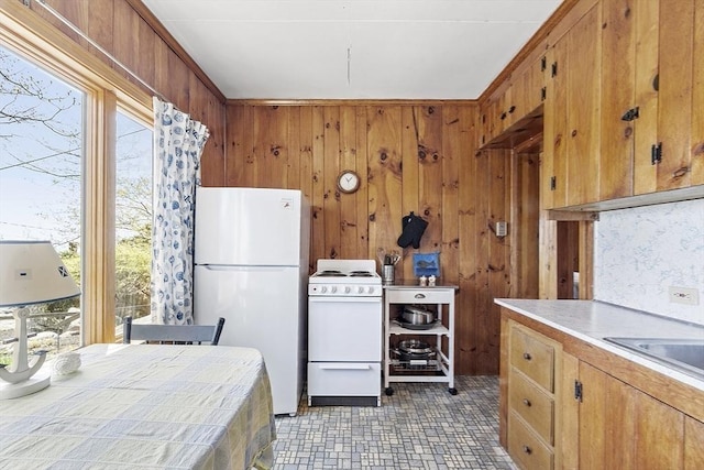 kitchen featuring white appliances, wooden walls, healthy amount of natural light, and brown cabinets