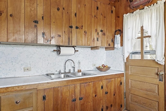 kitchen with a sink, brown cabinets, light countertops, and decorative backsplash