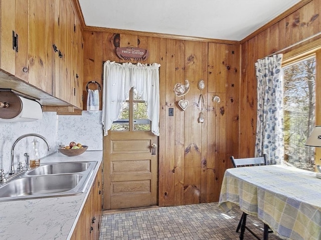 kitchen with a sink, brown cabinetry, light countertops, wood walls, and backsplash