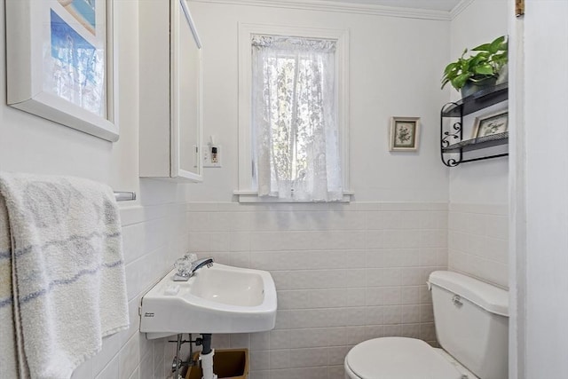 half bathroom with tile walls, toilet, a sink, and a wainscoted wall