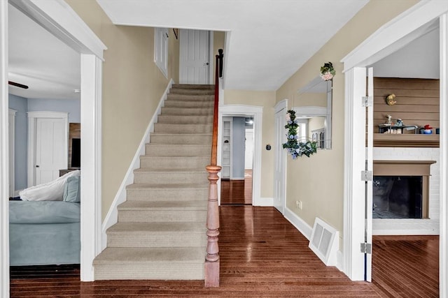 stairway featuring baseboards, visible vents, a fireplace with raised hearth, and wood finished floors