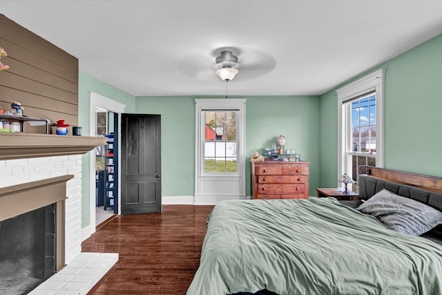 bedroom with baseboards, a brick fireplace, ceiling fan, and wood finished floors