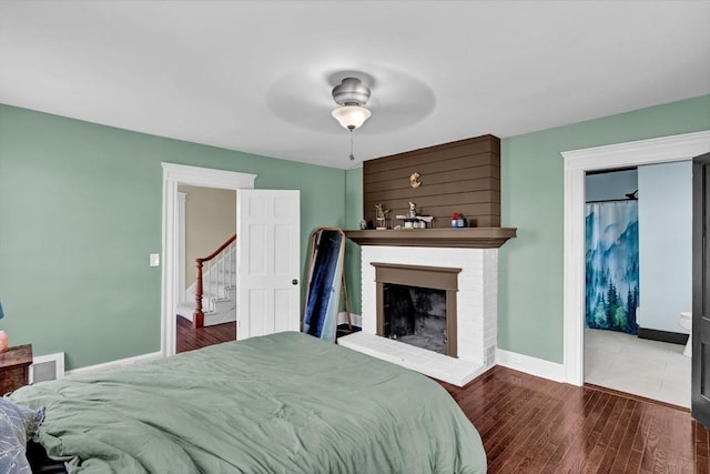 bedroom featuring a brick fireplace, baseboards, a ceiling fan, and wood finished floors