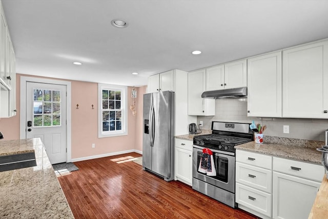 kitchen with stainless steel appliances, white cabinetry, dark wood-type flooring, baseboards, and under cabinet range hood