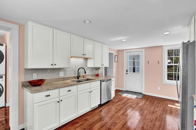 kitchen with baseboards, a sink, stacked washer and dryer, wood finished floors, and appliances with stainless steel finishes