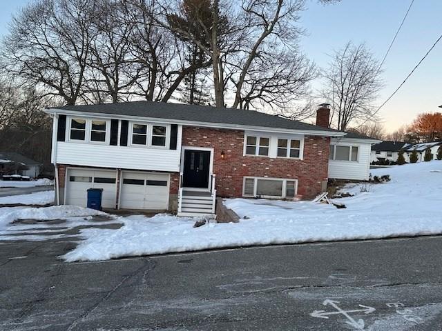 bi-level home featuring brick siding, a chimney, and an attached garage