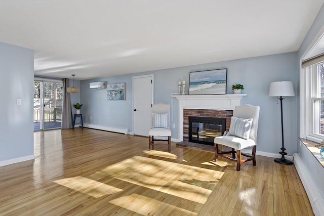 living area featuring baseboard heating, a fireplace, light hardwood / wood-style floors, and an AC wall unit